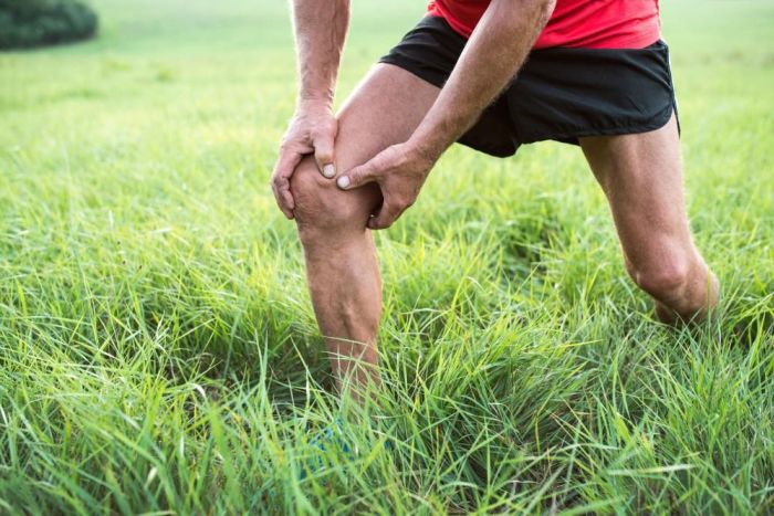 Man stretching and holding knee in grass